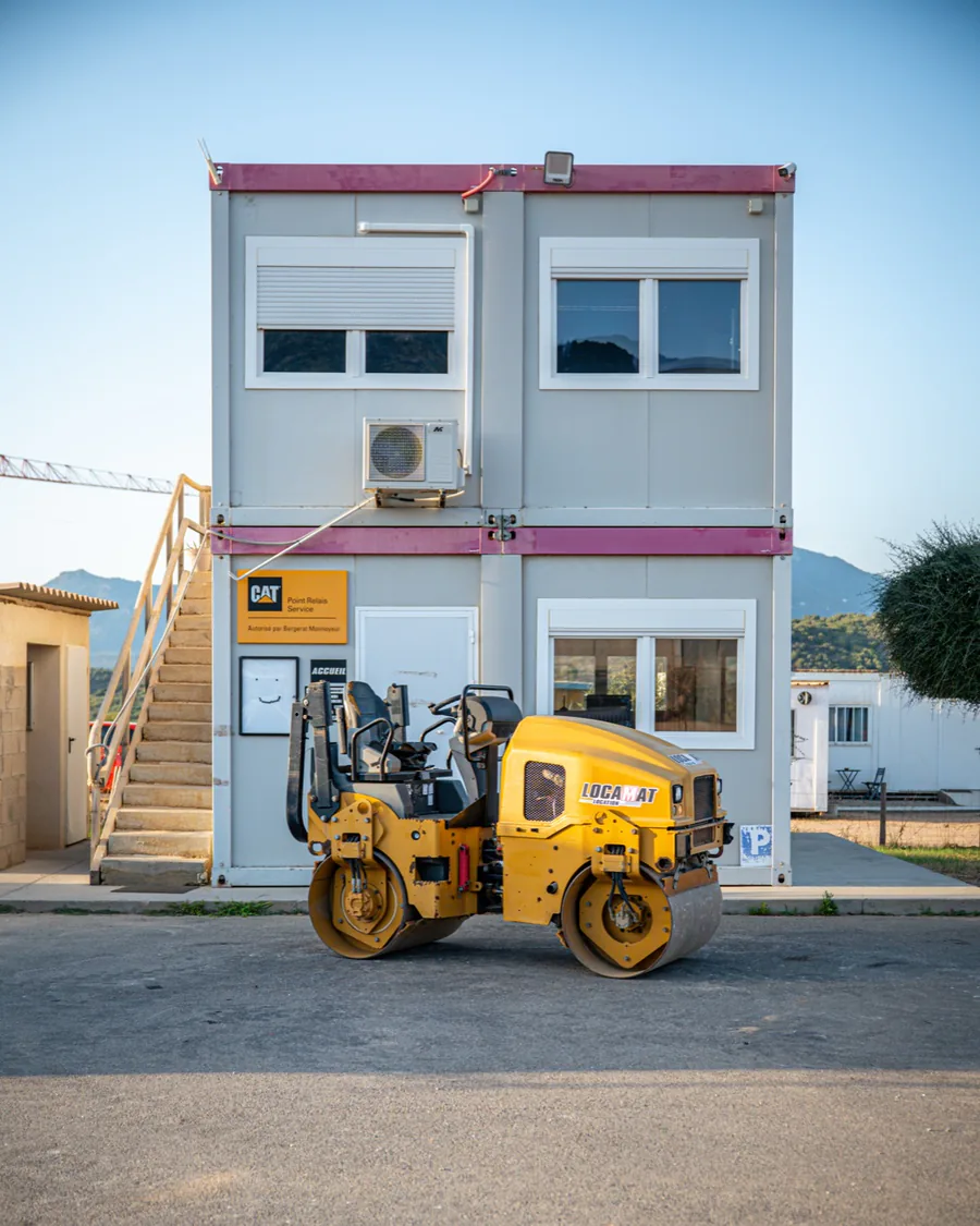 L'agence Locamat dans la zone industrielle de Tavaria à Propriano : le bâtiment, son escalier, le panneau « CAT Point Relais Service », et un compacteur Caterpillar devant.