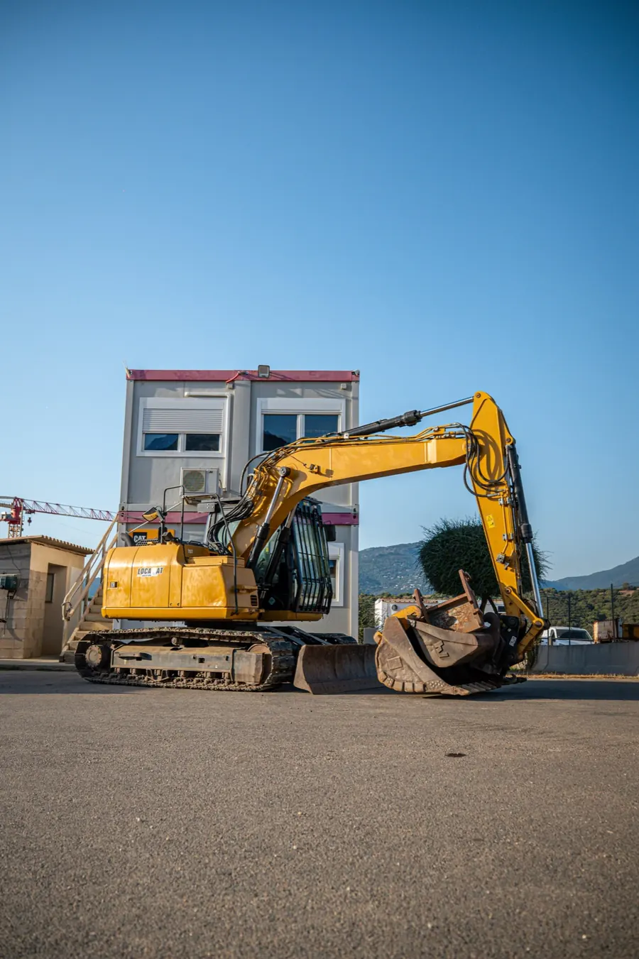 Une pelle Caterpillar garée devant l'agence Locamat, un bâtiment modulaire à deux étages, à Propriano.