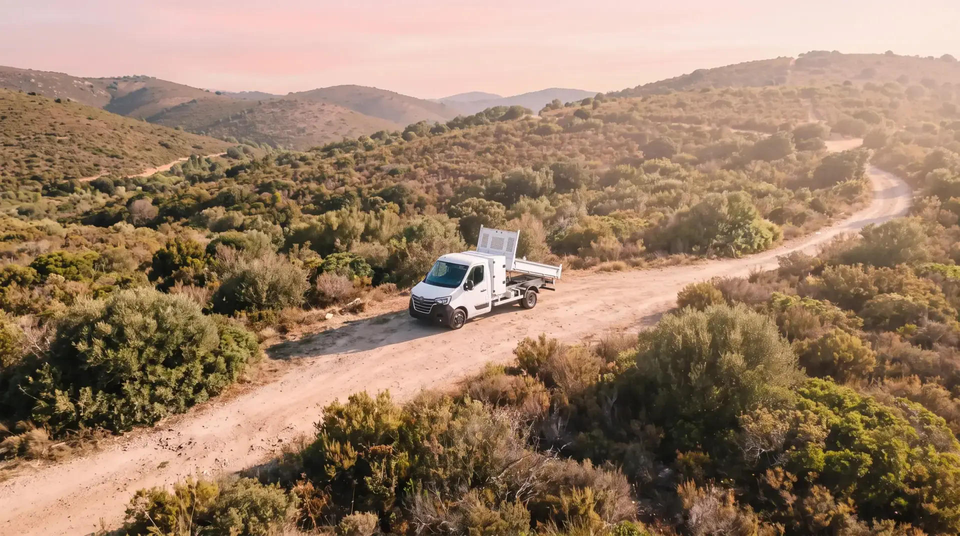 Un camion benne blanc sur une piste de terre au milieu du maquis, vu du ciel.