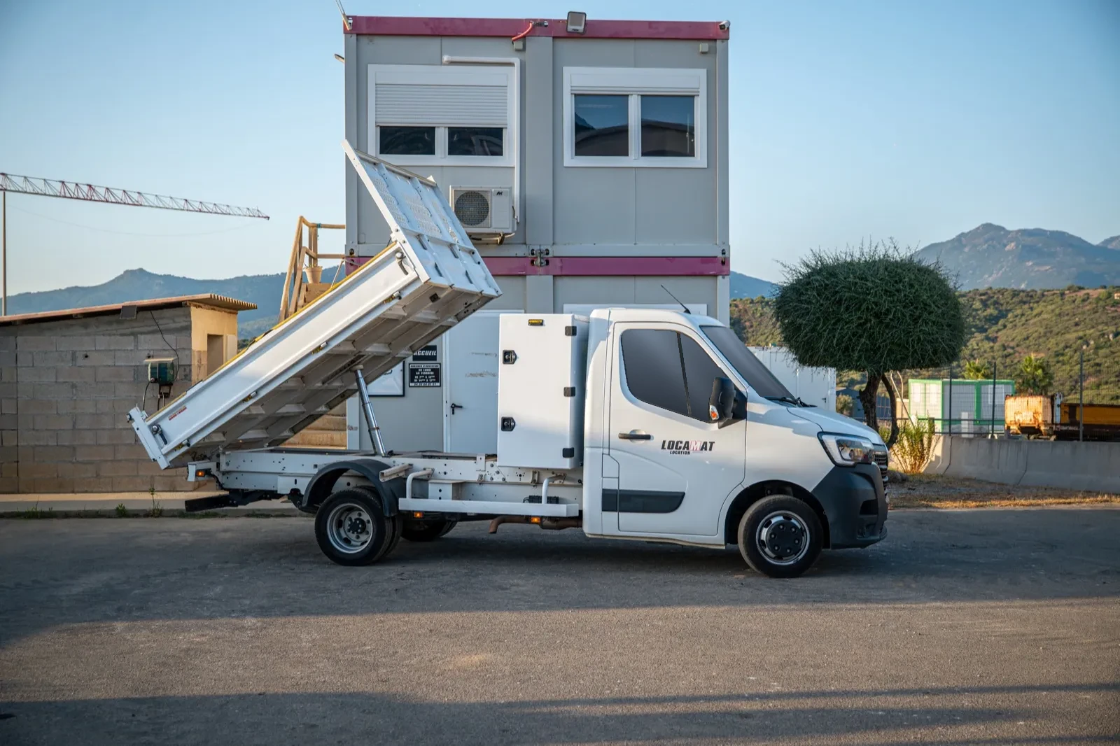 Camion benne 3,5 tonnes du parc Locamat, benne levée, de profil devant l'agence à Propriano.
