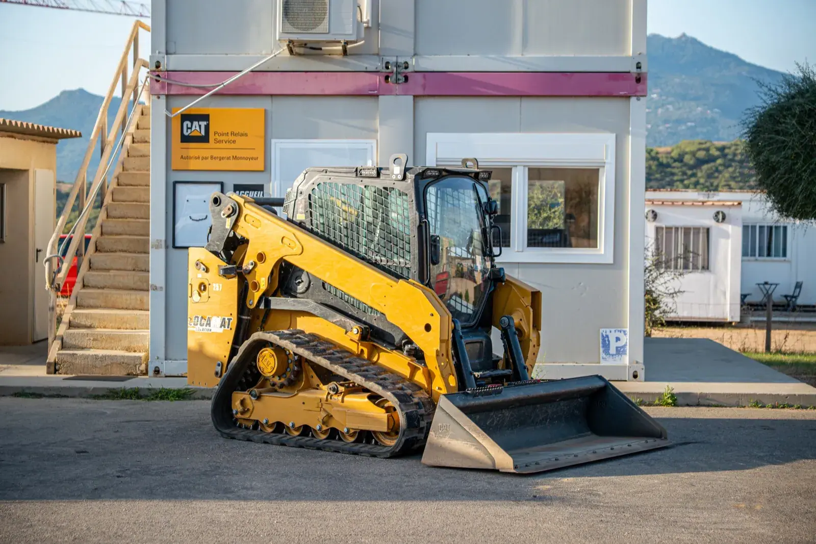 Mini-chargeur à chenilles du parc Locamat, godet au sol, devant l'agence.